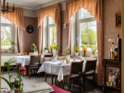 Restaurant mit eingedeckten Tischen und langen Vorhängen an den Fenstern