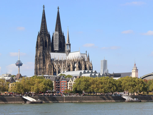 Im Zentrum der Kölner Dom und im Vordergrund der Rhein bei blauem Himmel